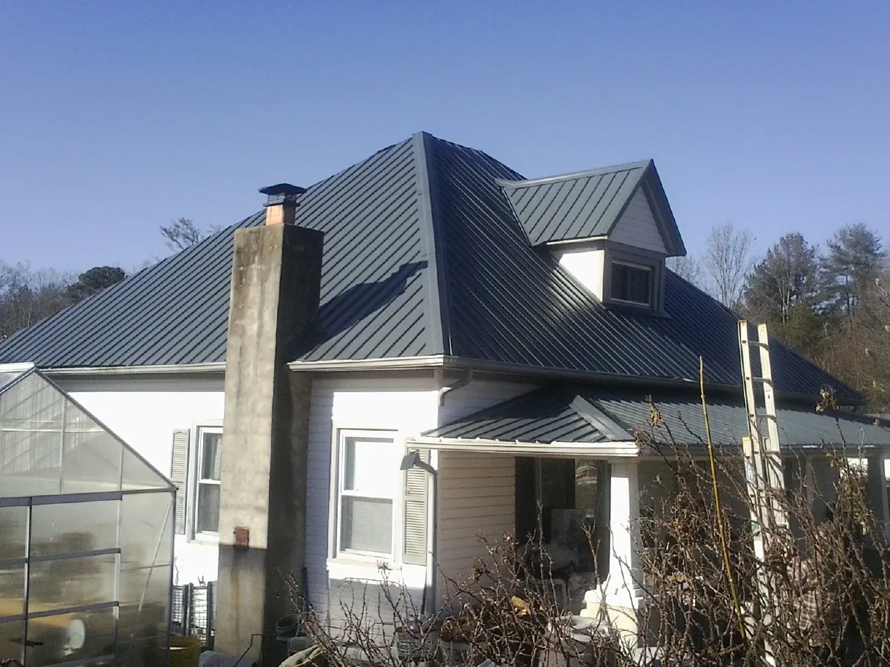 Dark blue standing seam metal roof on a white farmhouse with dormer — Slate & Tile Roof Repair by Roofing Brothers in Walthall