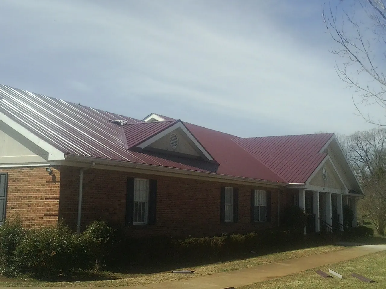 Red metal roof with gabled entries on a long brick building, from a Hail Damage Roof Repair job in Walthall