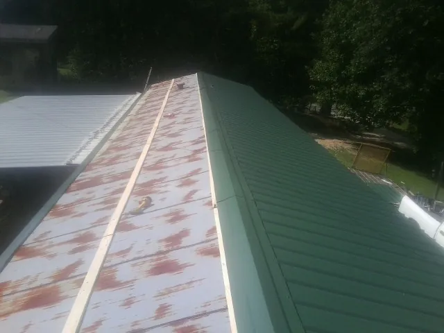 Old rusted panels beside newly installed green metal roofing — Wind Damage Roof Repair by Roofing Brothers in Walthall