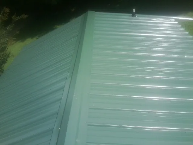 New green metal panels meeting at the ridge of a roof — Flat Roof Repair work by our crew in Walthall