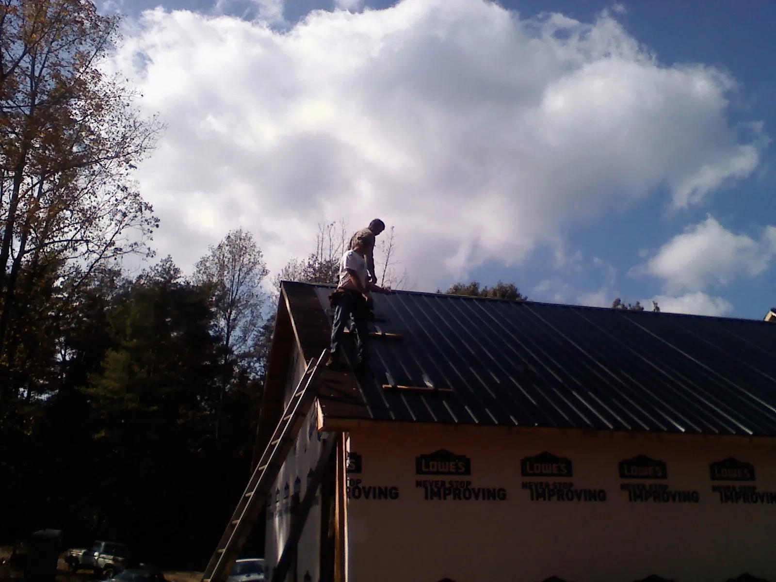 Roofer fastening dark metal panels high against a cloudy sky, from a Roof Inspection job in Walthall